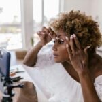 beauty trends and tips - A woman applying makeup while recording her beauty routine on smartphone indoors.