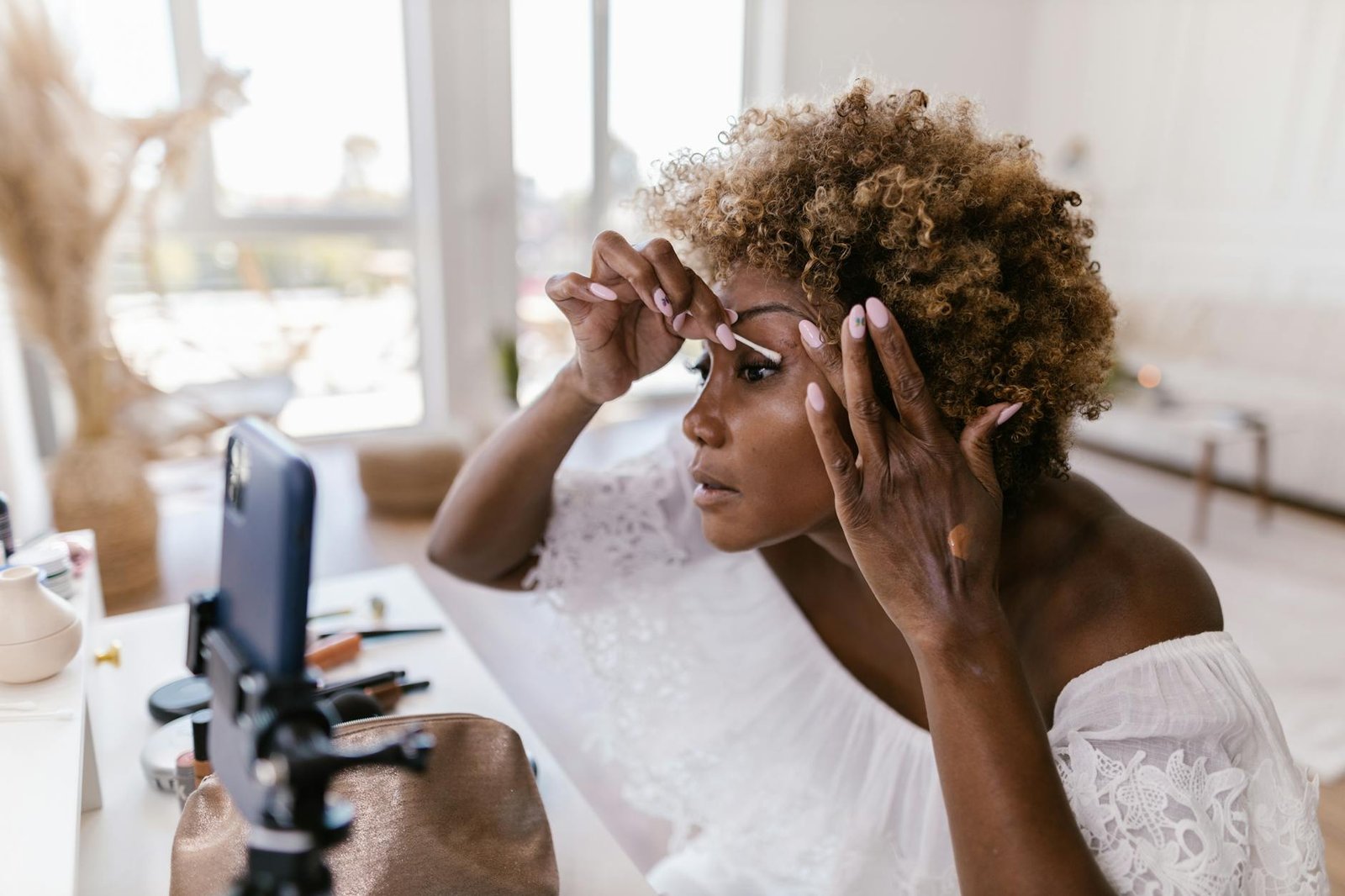 beauty trends and tips - A woman applying makeup while recording her beauty routine on smartphone indoors.