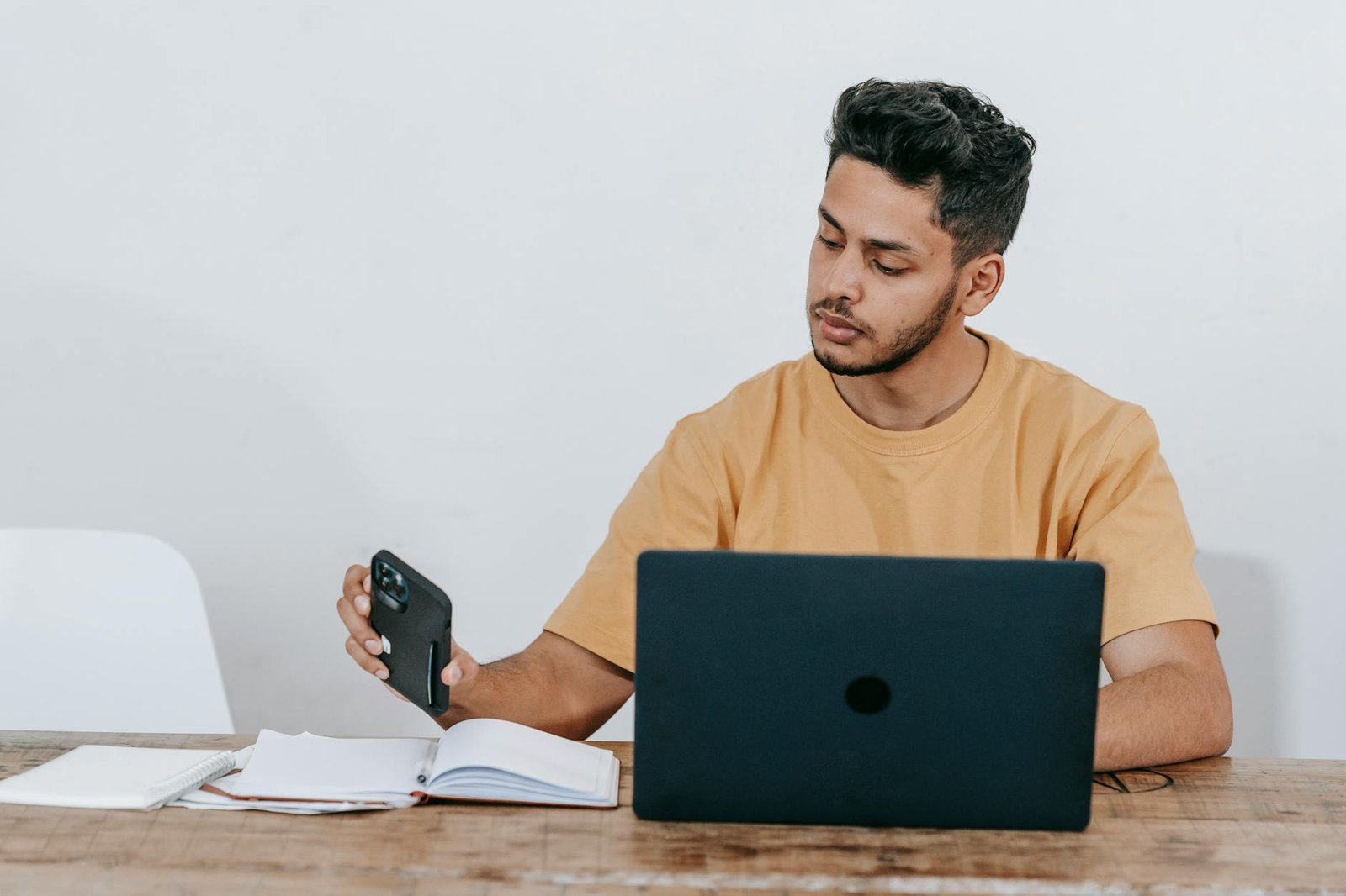 best gadgets for entrepreneurs - Serious young bearded Hispanic male entrepreneur in casual clothes checking notifications on mobile phone while working at table with laptop and notebook at workplace