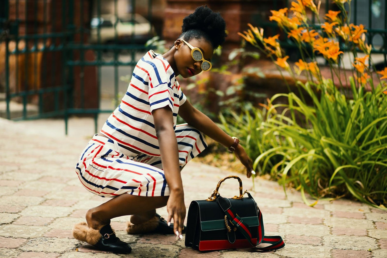 celebrity style inspiration - Stylish woman squatting outdoors with trendy striped outfit and designer bag. Vibrant and fashionable.