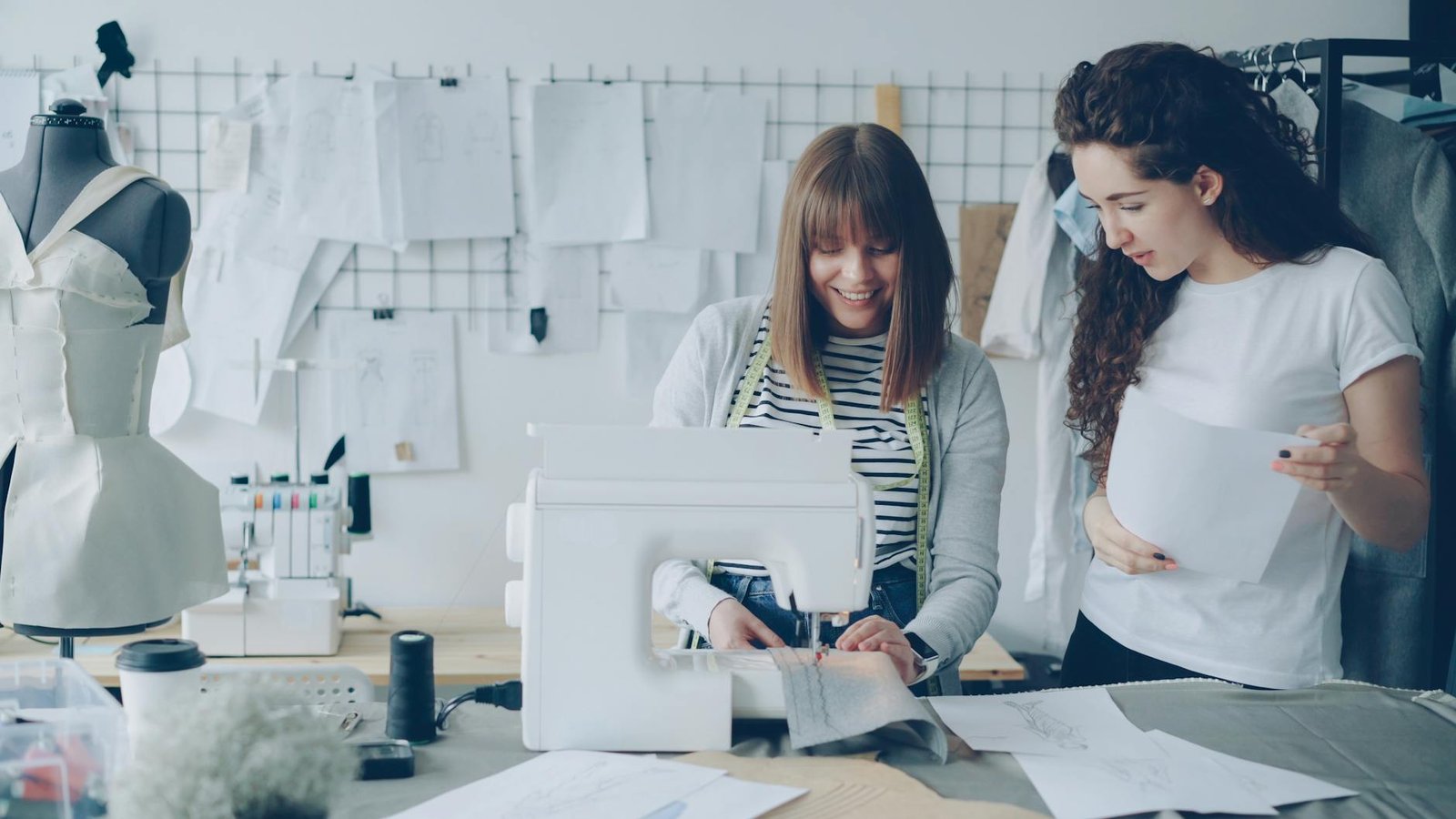 fashion career guides - Two women collaborating on sewing project in a fashion studio filled with sketches and materials.