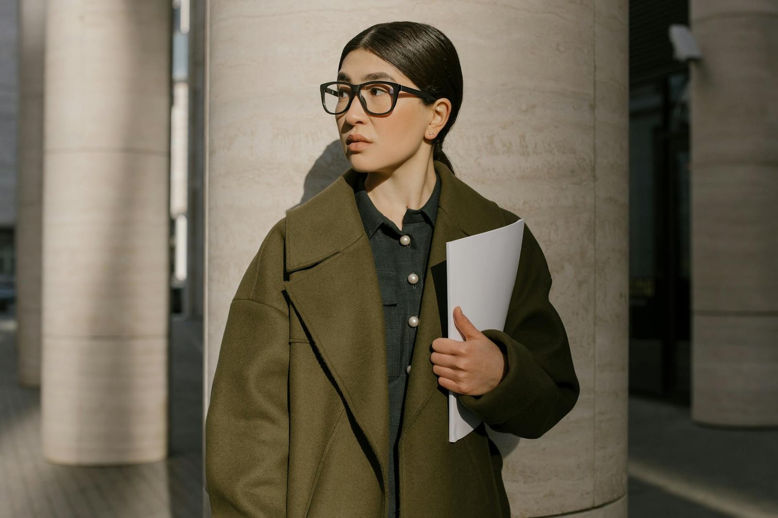 fashion career guides - A professional woman in a coat standing outside, holding papers and looking away thoughtfully.