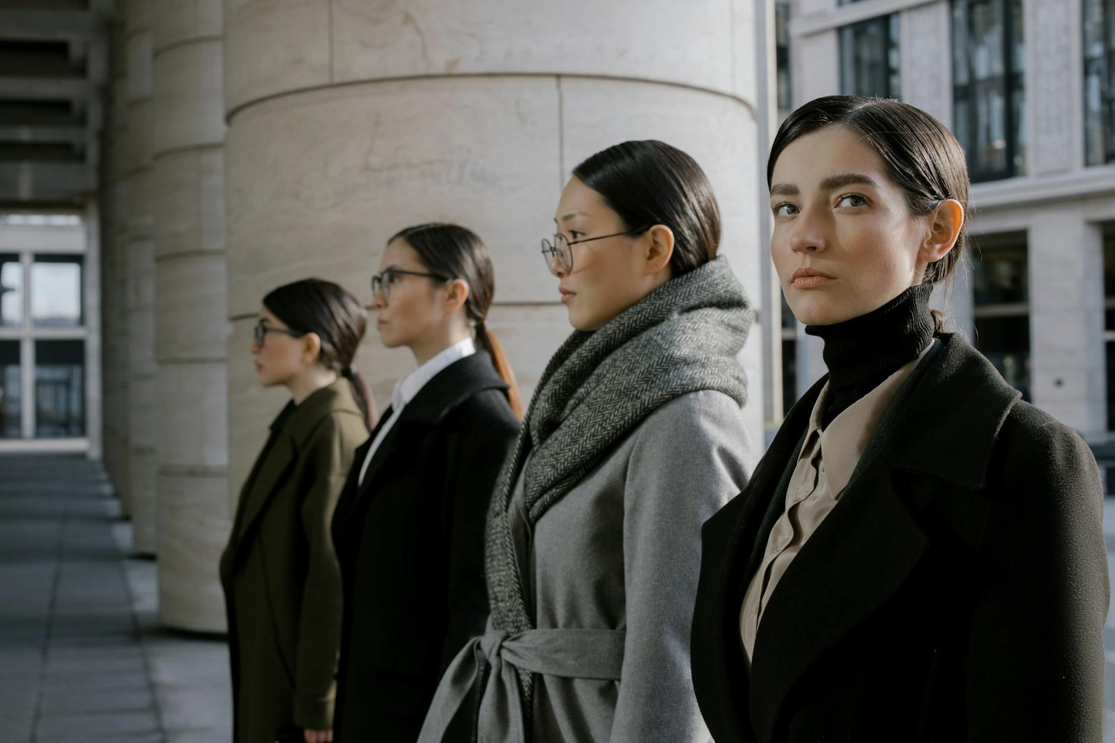 fashion career guides - Four professional women in elegant coats walking in an urban setting, showcasing diversity and style.