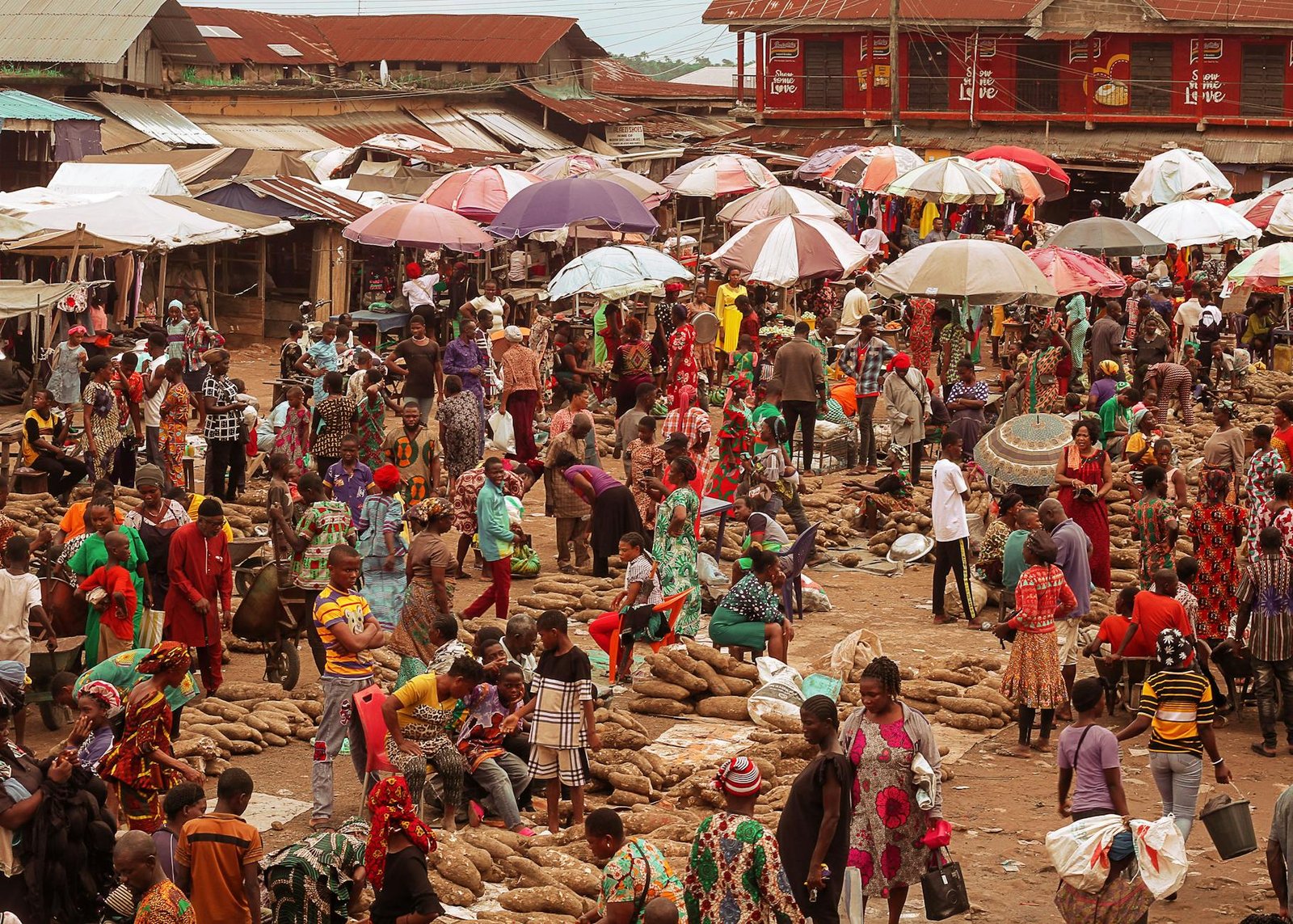 fashion culture and society - Lively outdoor African market with people selling goods under colorful umbrellas.