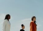 fashion trends for women - Three fashionable women in stylish blazers standing confidently under a clear sky.