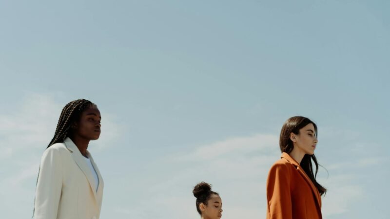 fashion trends for women - Three fashionable women in stylish blazers standing confidently under a clear sky.