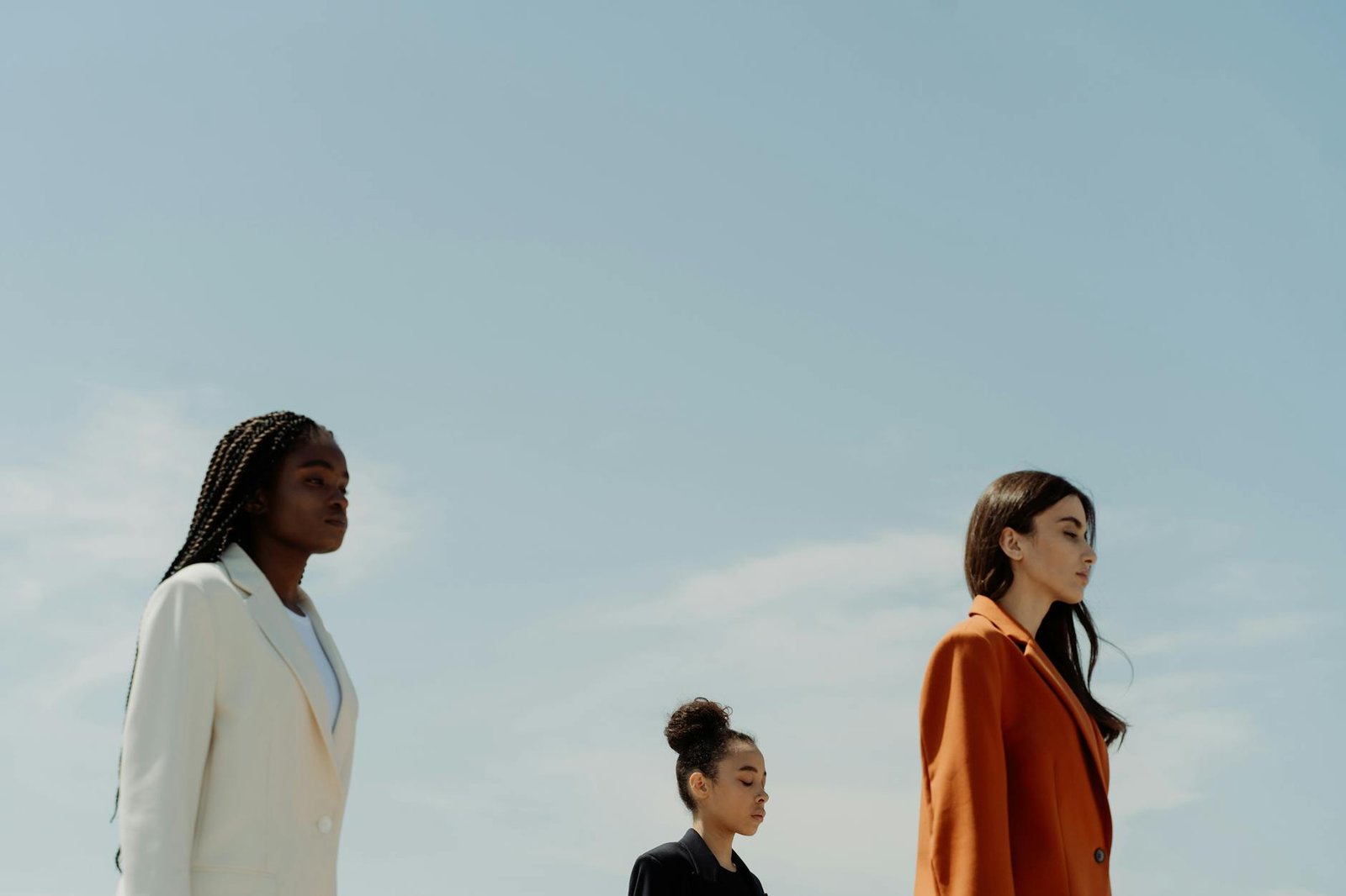 fashion trends for women - Three fashionable women in stylish blazers standing confidently under a clear sky.