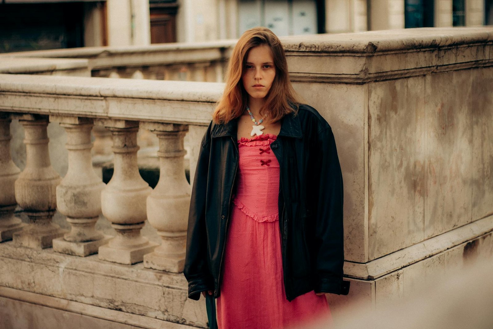 french style inspiration - Portrait of a young woman in pink dress and black jacket on an urban stone balcony in Marseille, France.