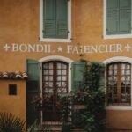 french style inspiration - Rustic French building facade with green shutters and climbing plants in Provence.