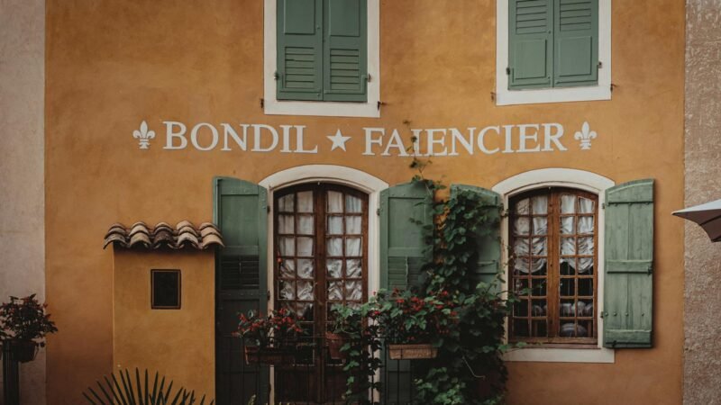 french style inspiration - Rustic French building facade with green shutters and climbing plants in Provence.