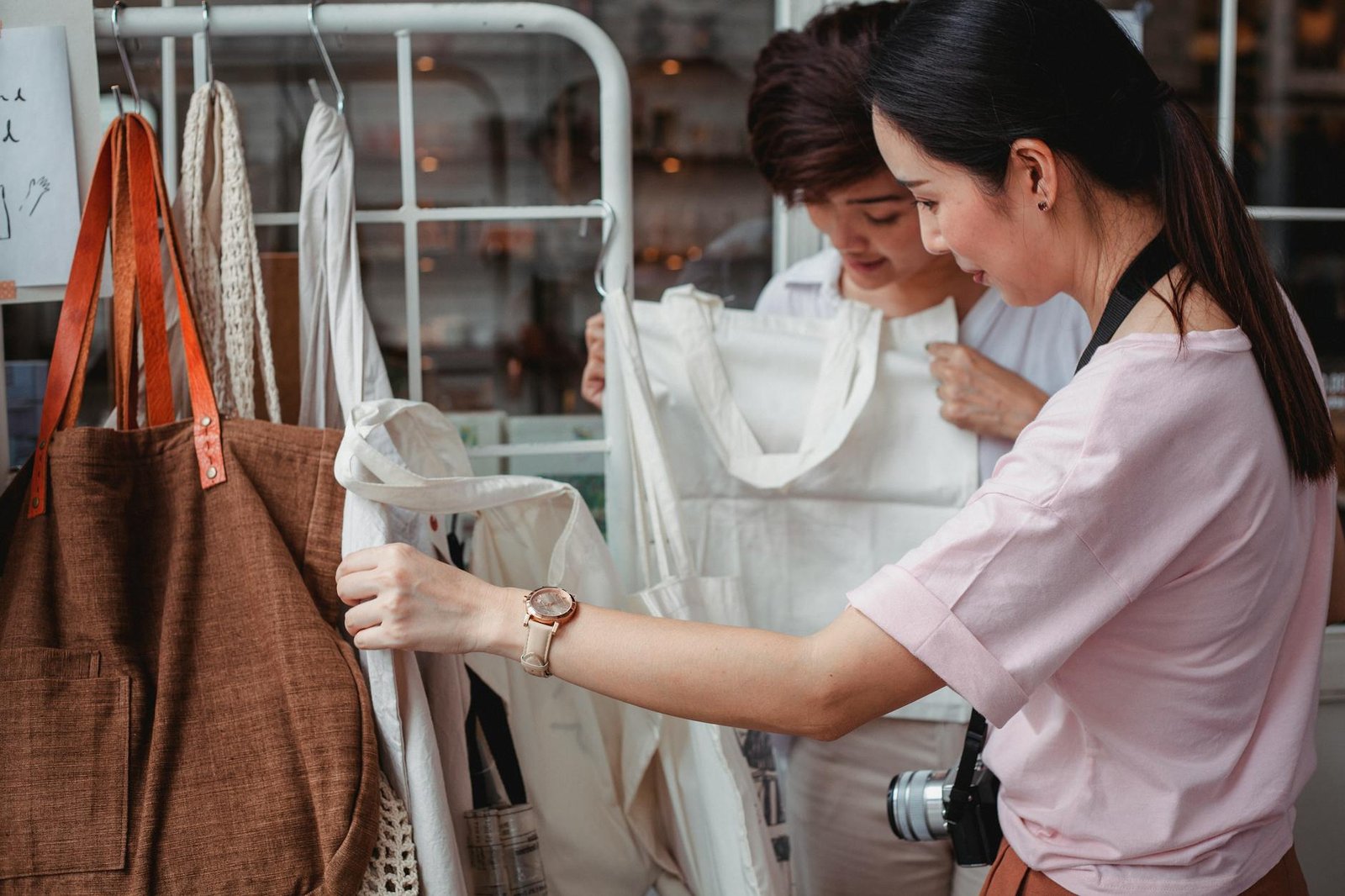 what is sustainable fashion - Side view of fashionable young ethnic female friends choosing stylish eco friendly cotton bags in boutique