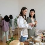 what is sustainable fashion - Four women browsing clothes and items at an indoor swap party, focused on sustainable living.
